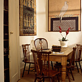 Kitchen with pine dining table and large Chinese prints on the wall assorted antique spindle back dining chairs and potted red orchid