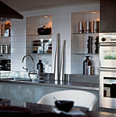 Küchendetail mit weißen Wandfliesen und eingelassenen Regalen sowie Zubehör und Herd aus Edelstahl