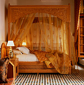 Ornate and decorative gold coloured bedroom with four poster bed with golden bed linen and voile drapes with tiled mosaic floor at the hotel Riad Myra in Fez Morocco