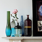 Row of coloured glass vases and bottles on a mantelpiece