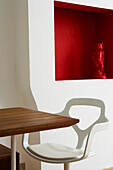 "Detail einer rot gestrichenen Nische mit passender gestiefelten Kater""-Statuette und modernem Plastik-Esszimmerstuhl"""