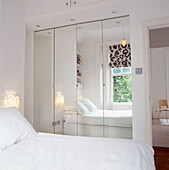 View of white bedroom reflected in mirrored wardrobe doors with