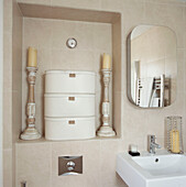 Close up of neutral stone wall tiles in bathroom with built in toilet cistern and candlesticks and three stacked boxes in the alcove