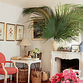 In the living room baskets of driftwood sit under a painted MDF table beside an ornate fireplace with a palm frond in a cream vase