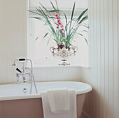 Roll top bath with shower attachment in cream painted tongue and groove bathroom a colourful display of pink orchids in a decorative sit on the window sill