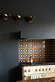 Detail of kitchen stove with Moorish wall tiles and sheep's head sculptures on a dark painted wall