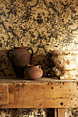 Detail einer Sammlung von Vintage-Töpferwaren auf einer alten Werkbank vor einer Chinoiserie-Tapete