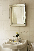 Waschbecken im Badezimmer mit Marmorwandfliesen und venezianischem Spiegel