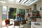 Glass table in London kitchen extension with view through sliding doors to garden, England, UK