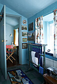 A bright blue bathroom has become a gallery of naive landscape and nautical paintings