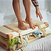 Junge Frau steht auf einem überfüllten Koffer auf einem Bett
