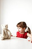 Young girl in red dress sits looking at her teddybear