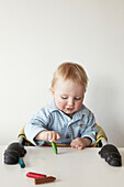 Two year old boy sits in high chair drawing with crayons