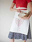 Low section woman in heart shaped apron holding a mixing bowl