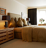 Luxury bedroom in gold decor with cushions and padded headboard and black bedside lamps