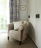 Bedroom corner decorated in soft pastel colours with upholstered armchair and patterned purple curtains