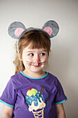 Kleines Mädchen mit lila T-Shirt, das sich eine Mäusemaske aufsetzt