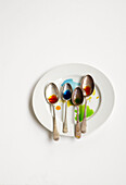 White plate with four spoons with coloured dye on