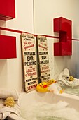 Bathroom detail with Ear Piercing sign and rubber duck and red cabinet
