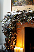 Open fire with large festive garland draped over the mantlepiece and candles burning on the hearth