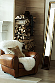 brown leather armchair with fur throw, narrow gilt mirror and a stack of firewood in luxury Zermatt home, Switzerland