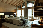 Double bed with matching lamps and armchairs in bedroom with open fire in luxury Zermatt home, Switzerland