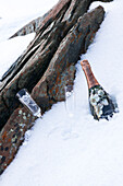Champagnerflasche und Flöten mit Felsen im Schnee am Berghang in Zermatt, Wallis, Schweiz