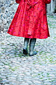 Low section of woman in red jacket and wellington boots walking in cobbled lane Cumbria, England, UK