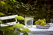 Glaskrug und Weintrauben auf Tisch mit Stuhl im Garten eines Londoner Stadthauses, England, UK