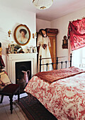 Weißes Kleid hängt an der Garderobe am Kamin im Schlafzimmer mit rot gemusterter Bettdecke in einem Haus in Evershot, Dorset, Kent, Vereinigtes Königreich