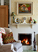 Armchair at open fire with shelf ornaments in London home, England, UK