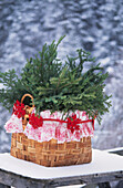Basket lined with festive paper filled with spruce branches and tied with a red garland