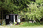 Schwarz gestrichenes Gartenhaus unter Bäumen in Rye, East Sussex, England, UK
