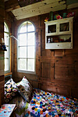 Sunlit arched window above patchwork bed cover in wood-panelled Rye treehouse, East Sussex, England, UK