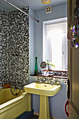 Yellow bath and sink at window of mosaic tiled bathroom of Hackney home, East London, UK