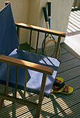 Blauer Regiestuhl mit Tennisschlägern und Sandalen auf einer Holzterrasse