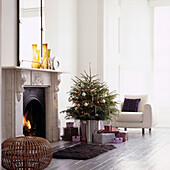 Sunlit white living room with Christmas tree and presents by lighted fire
