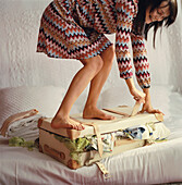 Frau im gestreiften Kleid steht auf einem überquellenden Koffer