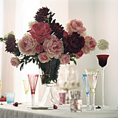 Large bouquet of Peonies in glass vase on a table top with decorative coloured wine glasses