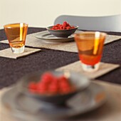 Bowls of raspberries and coloured glass on dining table with textured cloth