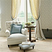 White armchair with cushion and footstool at French doors with co-ordinated curtains and wallpaper