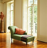 Green chaise longue in living room with polished floors French doors and a bust