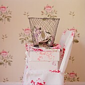 Offcuts of fabric in wastepaper basket on chair with floral wallpaper