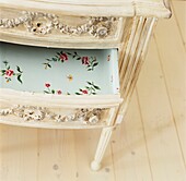Open drawer on chest lined with floral wallpaper