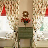 Symmetrical windows with floral print fabric on either side of a green painted bureau