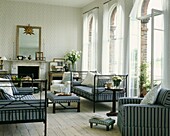 Striped upholstery co-ordinating furniture in living room with painted floorboards and high arched windows
