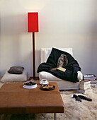 Hot water bottle and throw with books on armchair with red floor light and leather ottoman