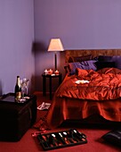 Backgammon-Set im lilafarbenen Schlafzimmer mit rot abgesetzter Bettdecke und Champagner