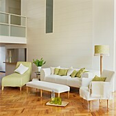 White sofa with cushions co-ordinating pastel green daybed in warehouse conversion with high ceilings and parquet floor