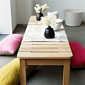 Cut flowers in vases on low wooden table with floor cushions